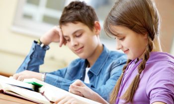 Portrait of teenage girl reading book with her classmate at background